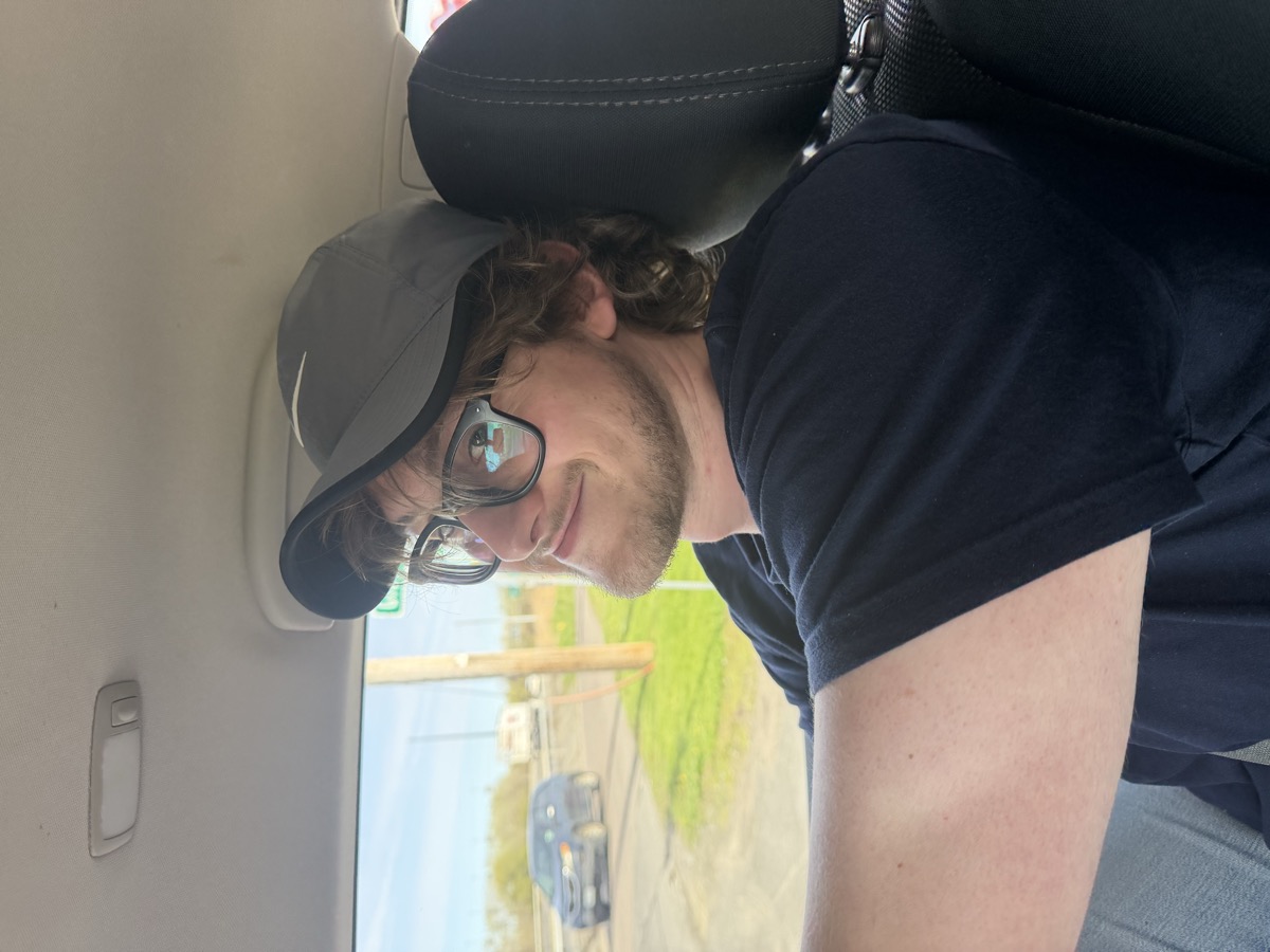 Eli Larkin grinning from the passenger seat in a Nike cap