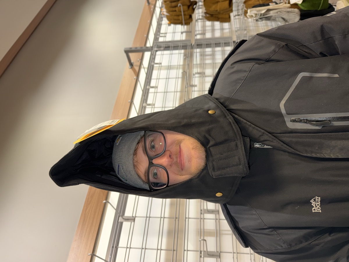 Eli Larkin trying on an enormous hooded coat in a store