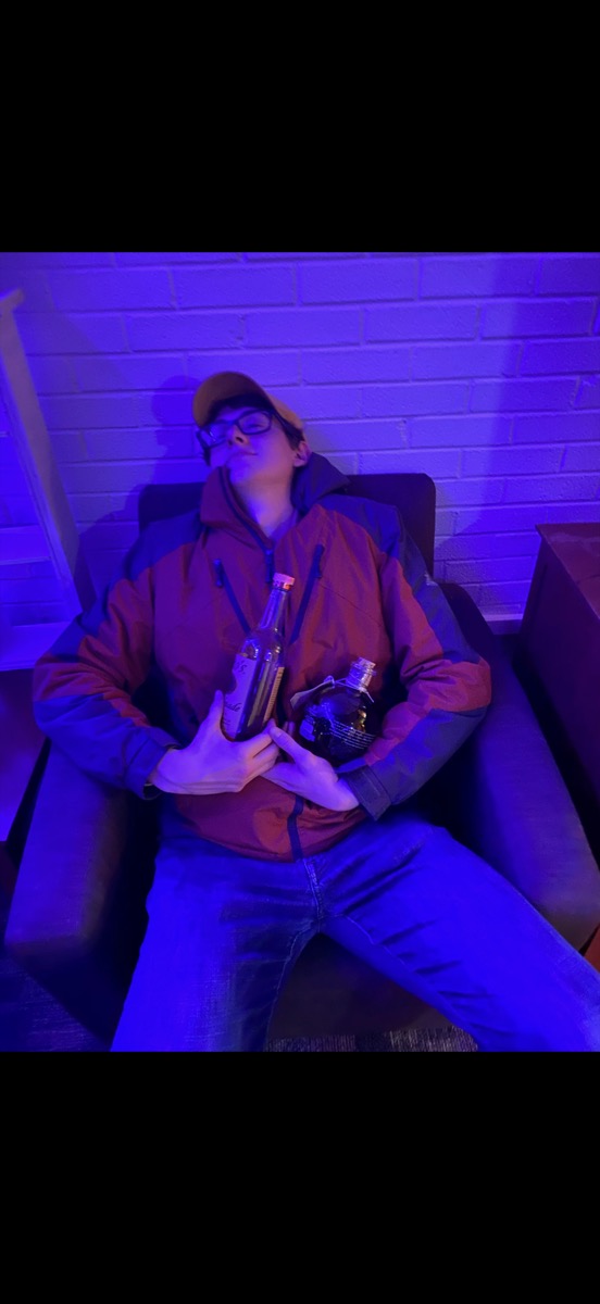 Eli Larkin reclined in an armchair under purple light holding two bottles